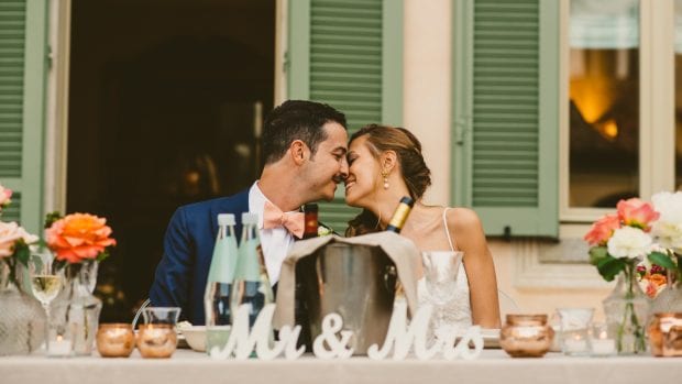 Gli sposi si scambiano un bacio romantico seduti al tavolo del ricevimento a Villa Bossi Varese.