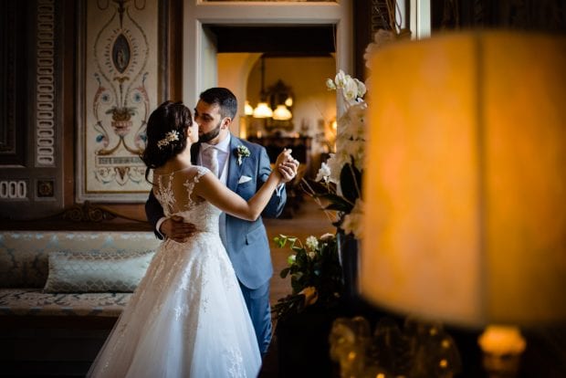 Gli sposi ballano dolcemente, illuminati dalla luce calda di una finestra di Villa Bossi.