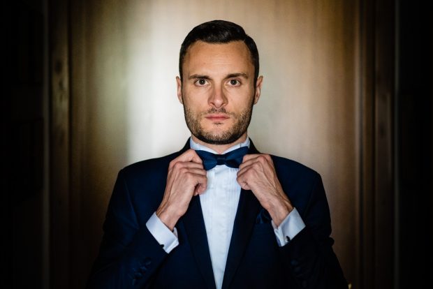 Lo sposo si sistema il papillon con sguardo determinato, pronto per il grande momento.