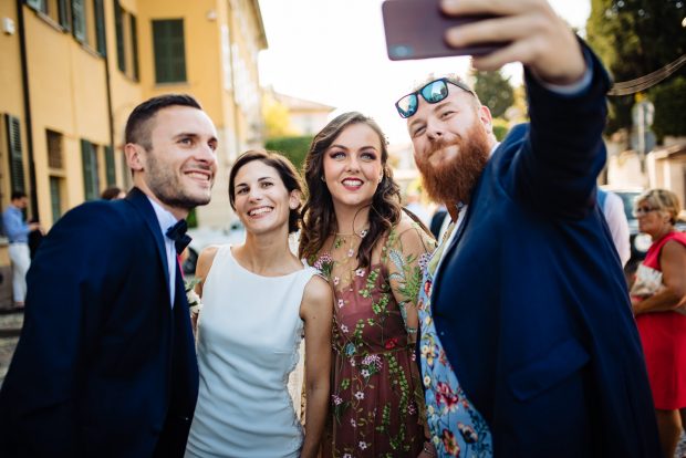 Gli sposi scattano un selfie con gli amici sorridenti, catturando un momento di gioia e complicità.