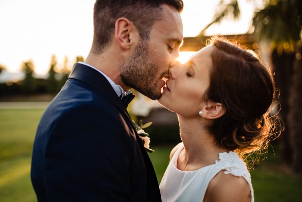 Gli sposi si scambiano un bacio romantico mentre il cielo si tinge di colori caldi al tramonto.