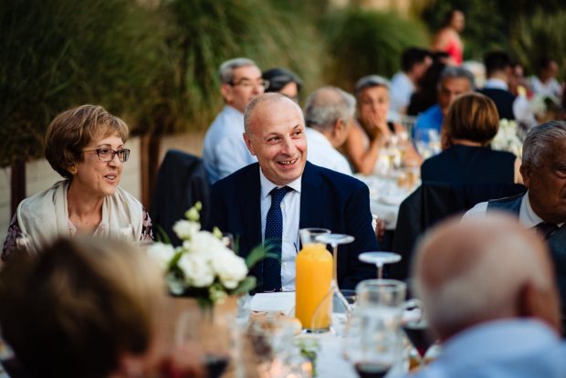 Il padre dello sposo ride felice durante la cena del matrimonio, circondato da amici e parenti.