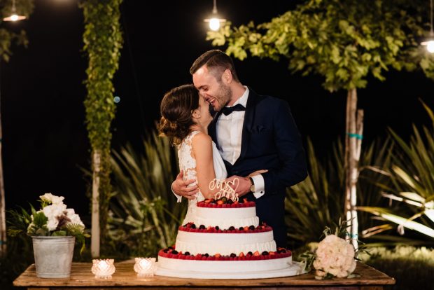Gli sposi si scambiano un bacio romantico subito dopo il taglio della torta, circondati dalla luce e dalla festa.