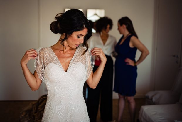 La sposa, emozionata, indossa il suo abito con l’aiuto delle amiche e dei familiari.