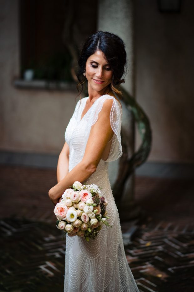 La sposa stringe tra le mani il suo bouquet floreale, realizzato con fiori freschi e armoniosi.