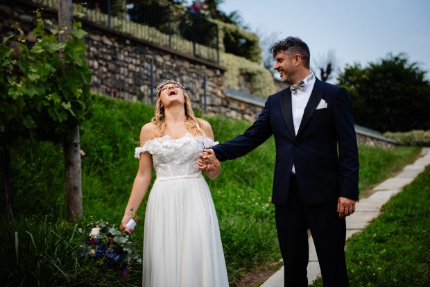 Gli sposi camminano tra i vigneti di Villa Calchi mentre la sposa ride felice, un momento spontaneo del reportage matrimoniale. Fotografo matrimonio Varese Villa Calchi.