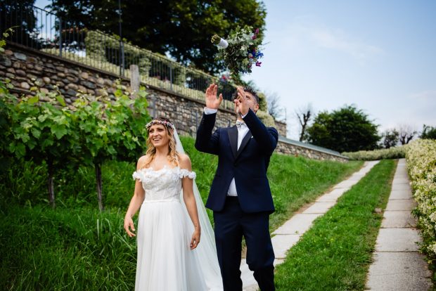 Lo sposo prende al volo il bouquet mentre passeggia con la sposa tra i vigneti di Villa Calchi, un momento divertente del matrimonio. Fotografo matrimonio Varese Villa Calchi.