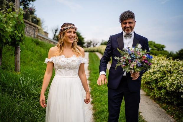 Lo sposo tiene il bouquet mentre passeggia tra i vigneti con la sposa, un dettaglio unico del matrimonio a Villa Calchi. Fotografo matrimonio Varese Villa Calchi.