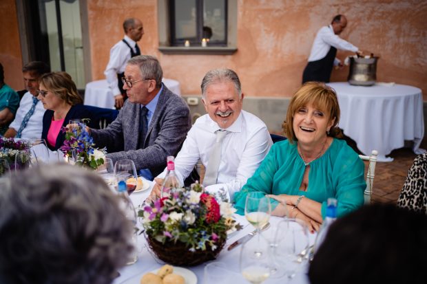 Il padre dello sposo ride di cuore al tavolo, condividendo momenti di gioia al matrimonio a Villa Calchi. Fotografo matrimonio Varese Villa Calchi.