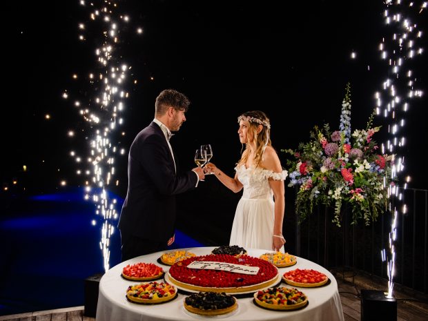 Gli sposi brindano davanti alla torta, illuminati dalle fontane fredde, in uno spettacolare scatto a Villa Calchi. Fotografo matrimonio Varese Villa Calchi.