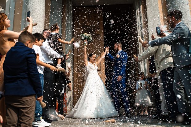 Gli sposi sorridono mentre gli invitati lanciano il riso all’uscita dal Santuario Santo Crocifisso, catturati da un fotografo matrimonio Villa Antona Traversi.