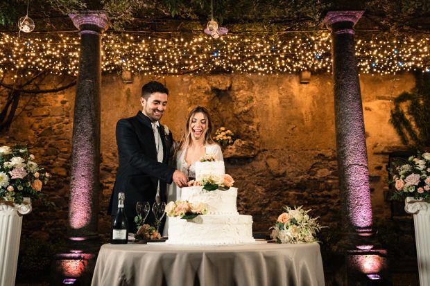 Marika e David sorridenti mentre tagliano la torta nuziale durante il ricevimento serale