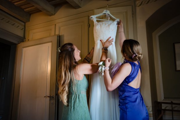 Patrizia che indossa il suo abito da sposa con l'aiuto delle amiche. Scatto realizzata da Paolo Lamperti Photographer Fotografo matrimonio Varese e Tenuta Frizzoni.