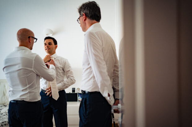 Lo sposo e i suoi amici alle prese con il nodo della cravatta prima del matrimonio a Villa Gaia Gandini.